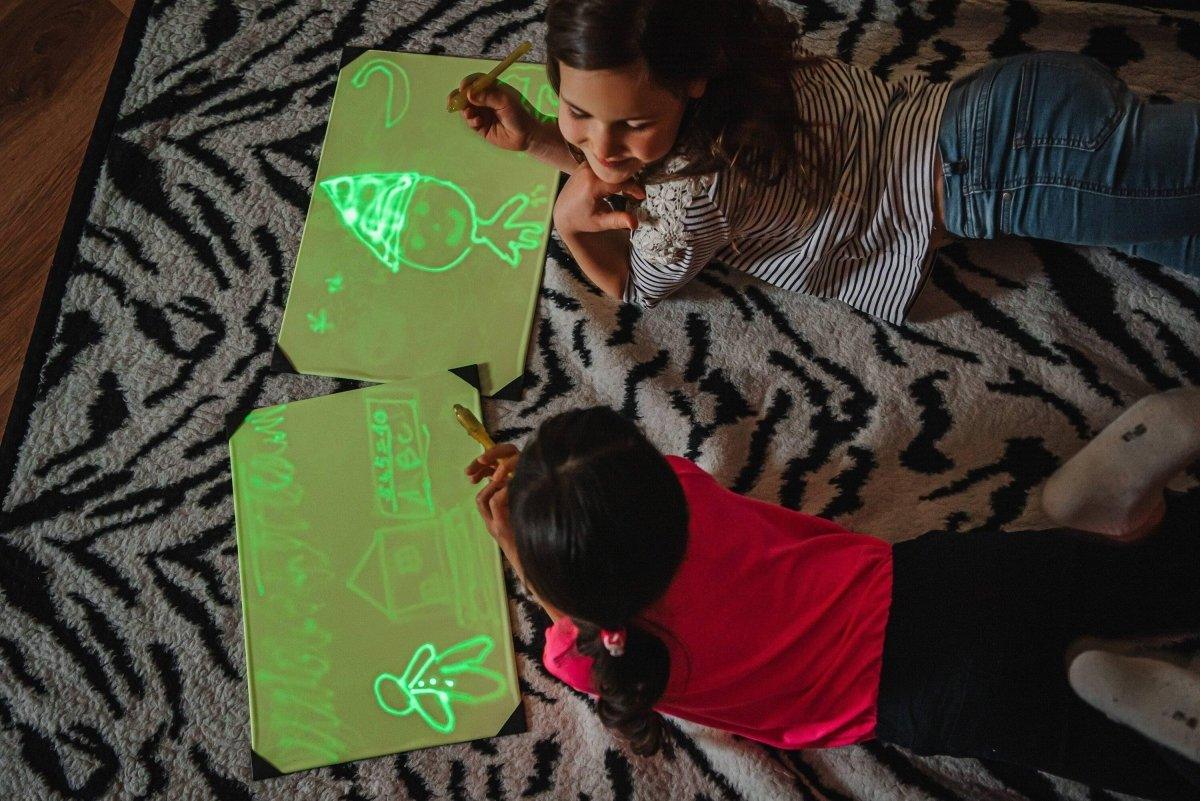 Two children drawing on illuminated sketch boards with glowing neon designs, showcasing creative play and imagination.