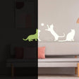 Glow in the dark cat wall decal on a beige wall above a couch with pillows.