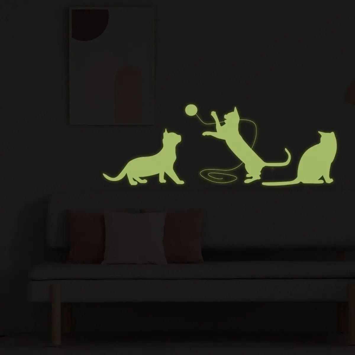 Glow in the dark feline wall decal featuring playful cat silhouettes on a dark wall above a sofa.