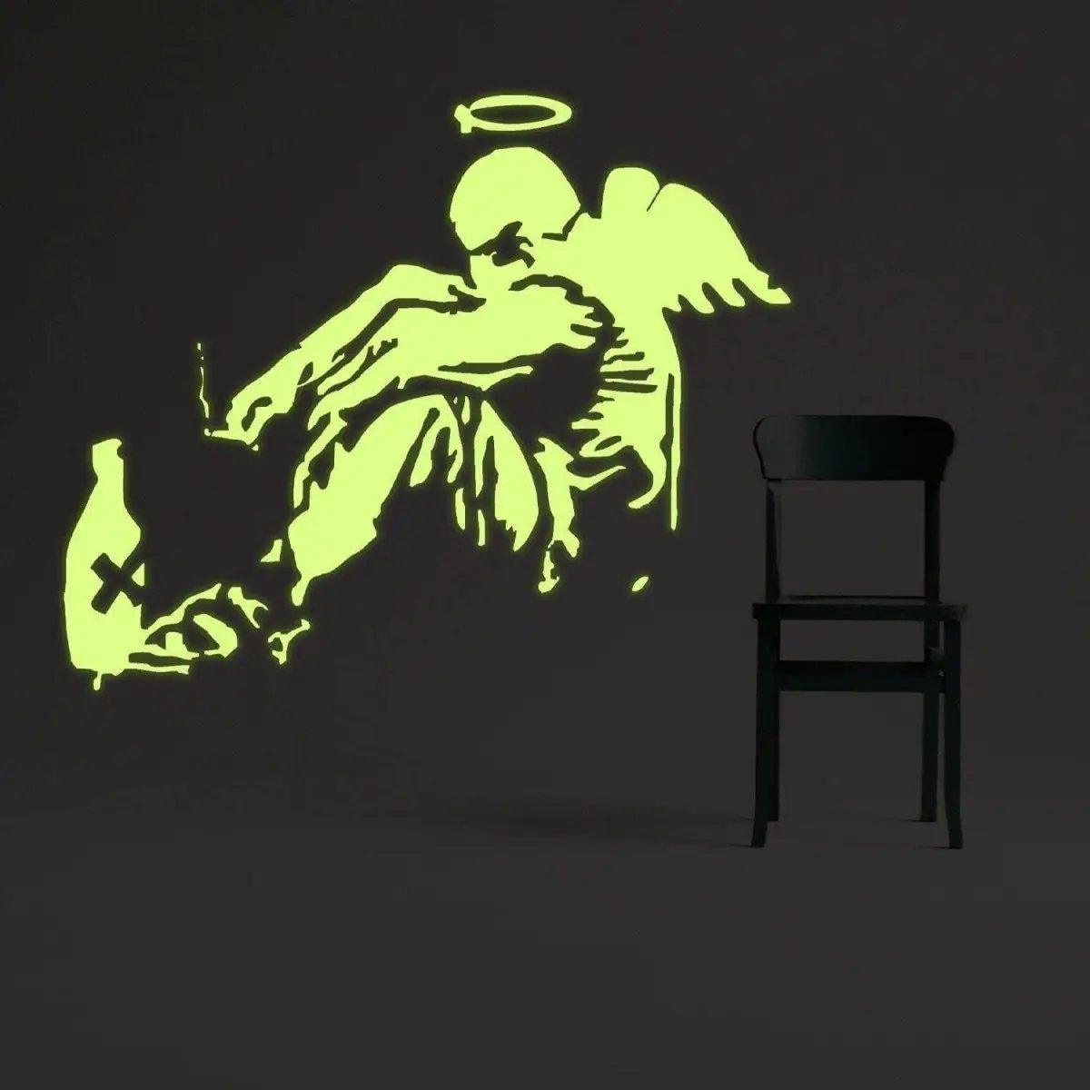 Glow-in-the-dark fallen angel wall decal illuminating a dark room beside a black chair.