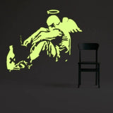 Glow-in-the-dark fallen angel wall decal illuminating a dark room beside a black chair.