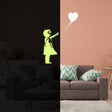 Luminescent girl silhouette with heart balloon wall decal glowing in a dark room over a cozy couch.