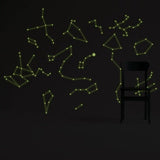 Glowing starry sky ceiling decals in green on a dark wall, featuring luminous constellation stickers with a chair.
